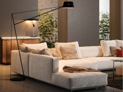 Una sala de estar moderna con un sofá modular de color claro, almohadas, una lámpara de pie y plantas en macetas de fondo. Perfecta para los entusiastas de la fotografía inmobiliaria que buscan capturar espacios acogedores.