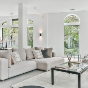 Moderna sala de estar con grandes ventanales con vista a la vegetación, con un sofá modular gris claro, una mesa de centro de vidrio y una decoración minimalista. Este espacio es perfecto para CAPTURAS de fotografía inmobiliaria.